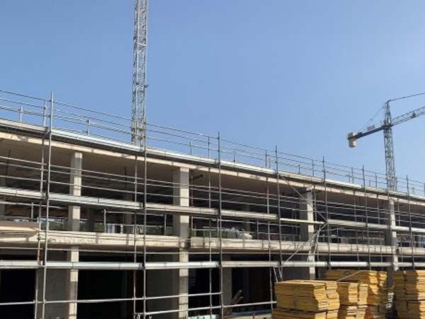 Sitio de construcción con andamios y grúas contra un cielo azul claro.