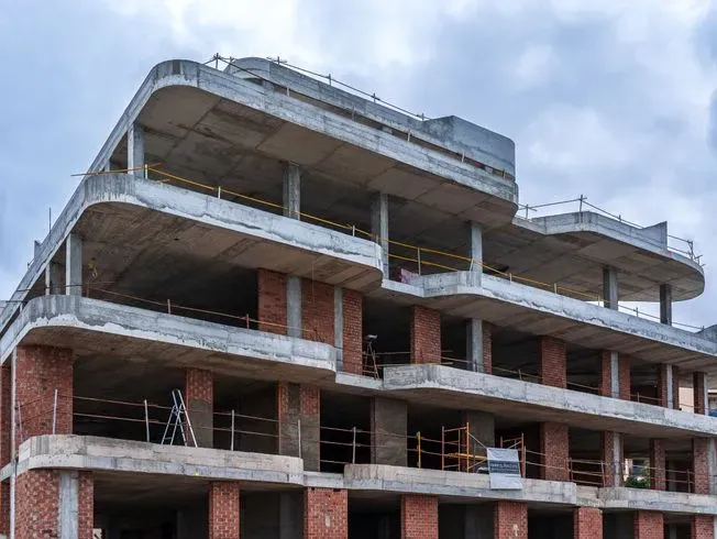 Edificio en construcción, pisos sin terminar, ladrillo y concreto, cielo nublado.