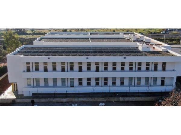 Edificio moderno blanco con paneles solares en el techo; vista exterior con luz natural.