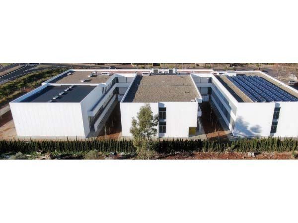 Edificio blanco moderno con techos planos, una hilera de paneles solares y una línea de vegetación.