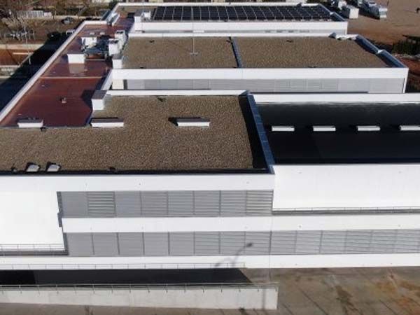 Edificio blanco con techos planos, paneles solares y ventilaciones horizontales grises.