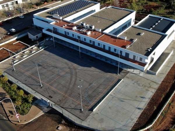 Vista aérea de un moderno edificio blanco con paneles solares en el techo y una amplia zona de estacionamiento.