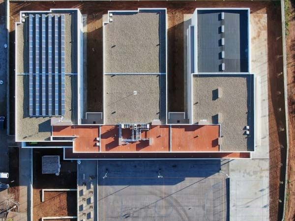 Vista aérea de un complejo de edificios con techos planos. Se ven paneles solares en un techo, grava y otros materiales.
