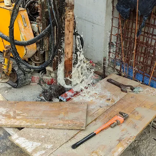 Taladro con pulverizador de agua, herramientas sobre tablones de madera en una zona de construcción.