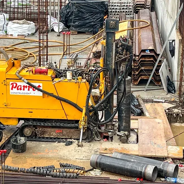 Perforadora Yellow Parrot en una obra, perforando el suelo. Hay tuberías y escombros cerca.