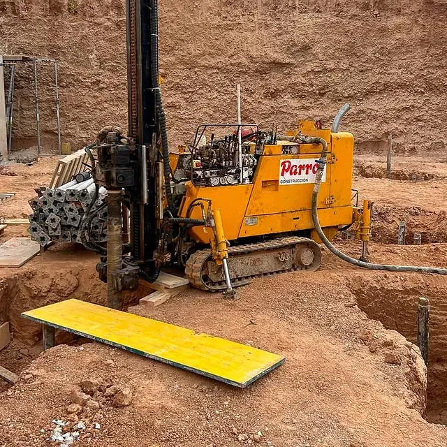 Máquina perforadora amarilla en un sitio de construcción, perforando tierra roja.
