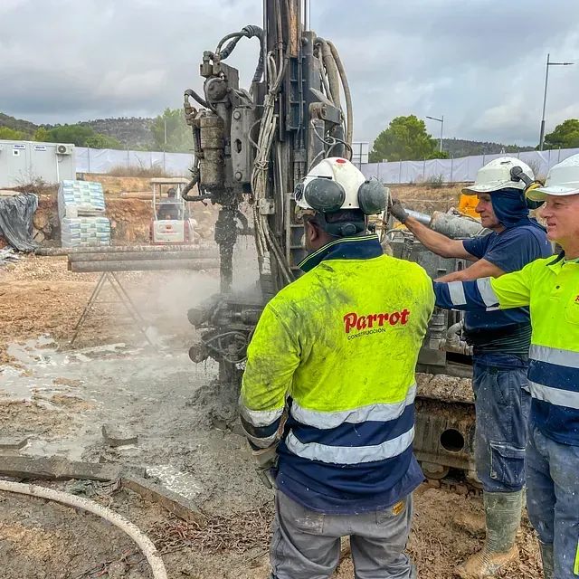 Obreros de la construcción operan una plataforma de perforación al aire libre. Uno lleva chaleco de seguridad, los demás cascos.