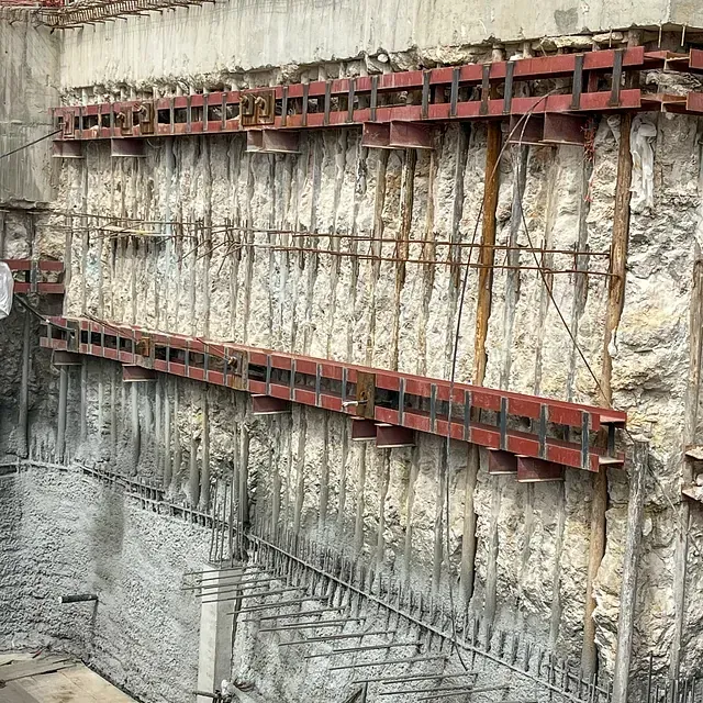Obra con muro de contención de hormigón, sostenido por vigas y barras metálicas de color rojo.