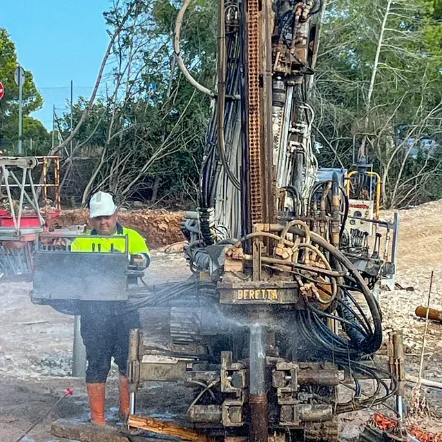 Un trabajador con chaleco de seguridad opera una máquina perforadora en un sitio de construcción.