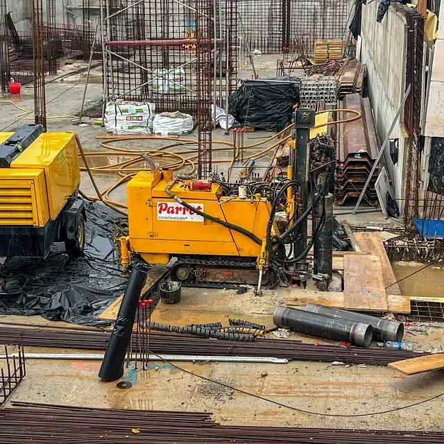 Máquina perforadora amarilla en un sitio de construcción con barras de refuerzo y equipos.