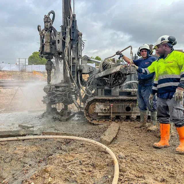 Los trabajadores de la construcción operan una máquina perforadora en un sitio de construcción fangoso.