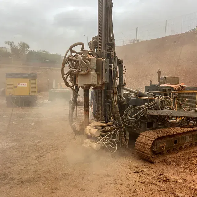 Una gran máquina perforadora levanta polvo mientras opera en un terreno fangoso.