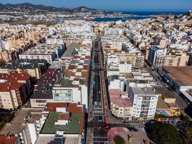 Vista aérea de un paisaje urbano con edificios, una carretera y el océano al fondo bajo un cielo despejado.