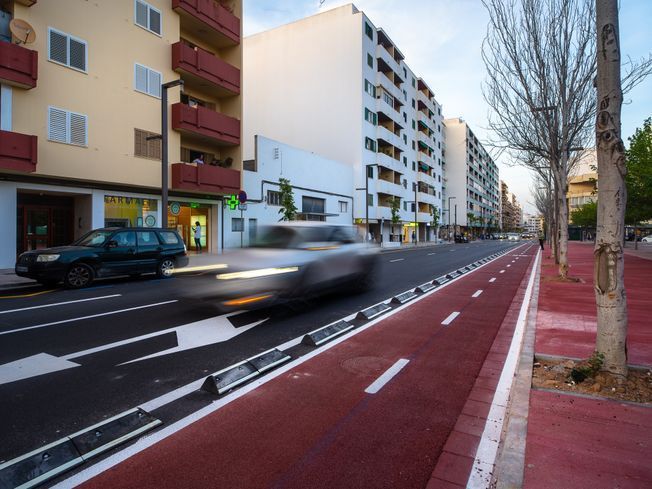 Escena callejera con automóvil borroso en el carril bici rojo, edificios, árboles y automóvil estacionado.