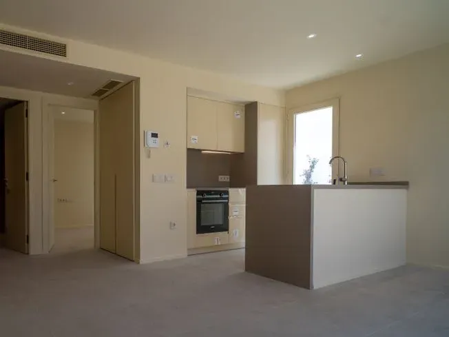 Cocina moderna vacía con isla, gabinetes beige, horno y una ventana.