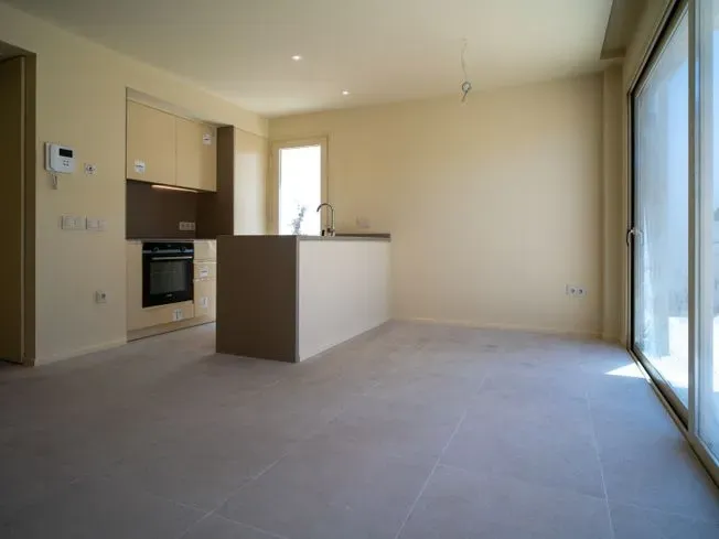 Cocina moderna vacía con isla, gabinetes de color beige claro y puertas corredizas de vidrio.