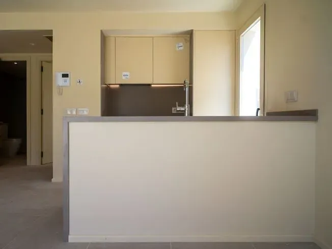 Cocina con muebles de color claro, encimera gris y media pared que da a la estancia.