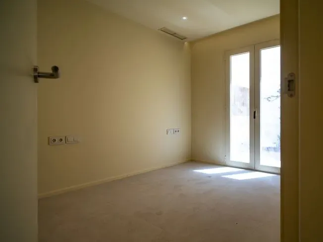 Habitación vacía con paredes beige, alfombra y puertas francesas, iluminación suave.