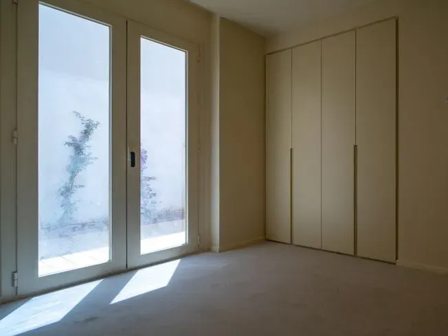 Habitación vacía con puertas de vidrio esmerilado, paredes de color claro, alfombra y un armario empotrado.