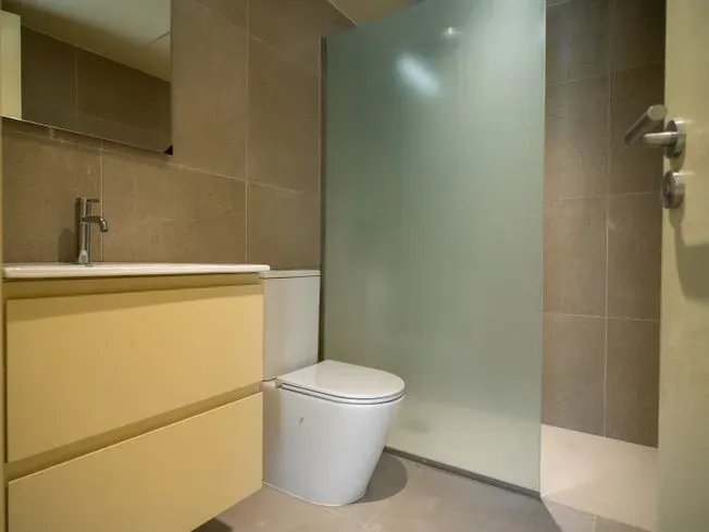Un baño moderno con un tocador de color amarillo claro, un inodoro blanco y una ducha de vidrio esmerilado.