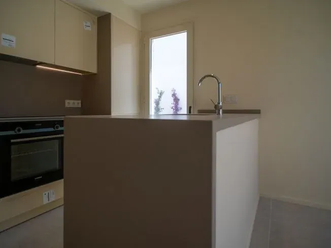 Cocina moderna con isla beige, fregadero y ventana.