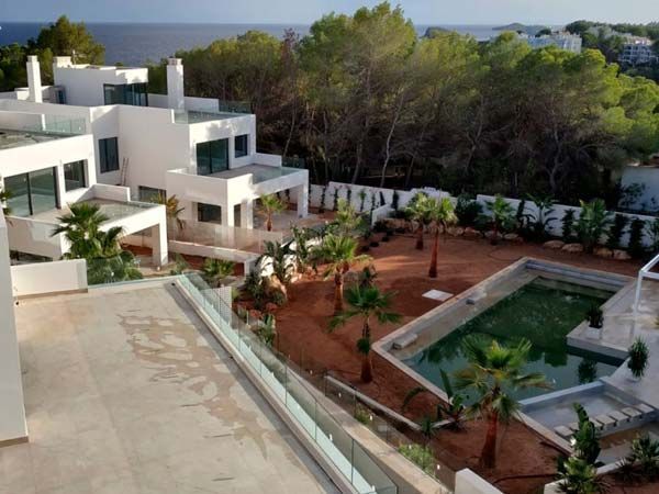 Villas blancas modernas con piscina, palmeras y vista al océano.