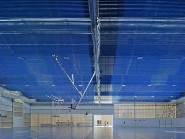 Pabellón deportivo interior con techo azul, paredes neutrales y suelo reflectante.