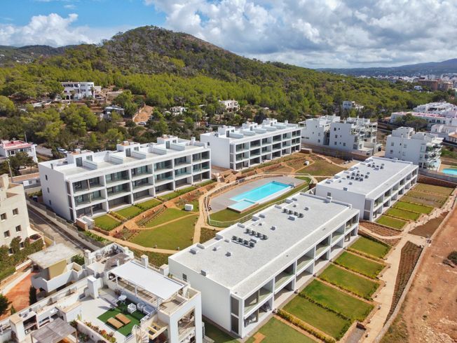 Vista aérea de modernos edificios de apartamentos blancos con piscina, cerca de una colina verde.
