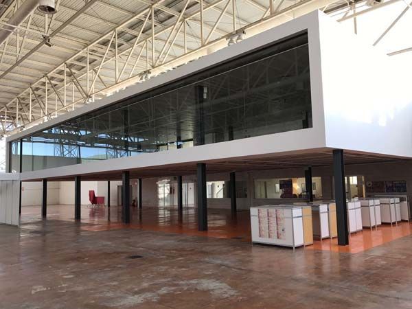 Moderno espacio de oficina con estructura elevada con paredes de vidrio dentro de un gran edificio industrial.