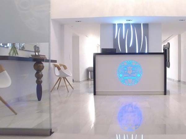 Recepción con escritorio blanco y logotipo iluminado en azul. Suelo de mármol.