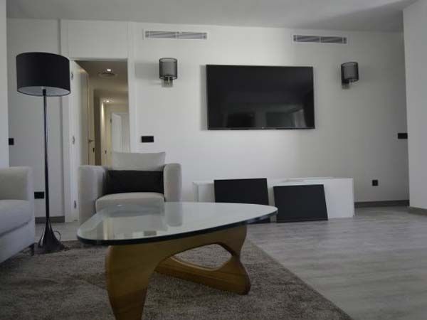 Sala de estar: TV, parlantes, sillón, mesa de café, alfombra y lámpara de pie contra paredes blancas.