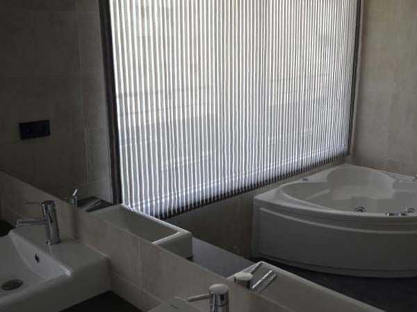 Baño moderno con bañera de hidromasaje y tocador, ventana con persianas.