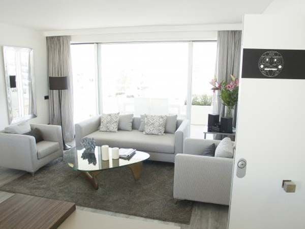 Una sala de estar luminosa con muebles gris claro, una ventana grande y una alfombra.