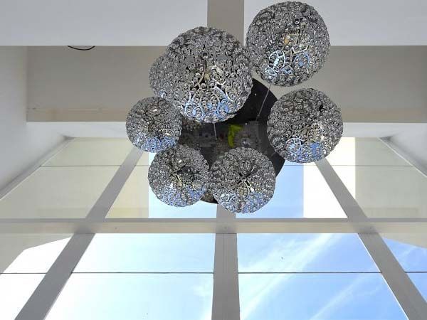 Una lámpara de araña de cristal cuelga delante de una ventana alta desde la que se puede ver un cielo azul.