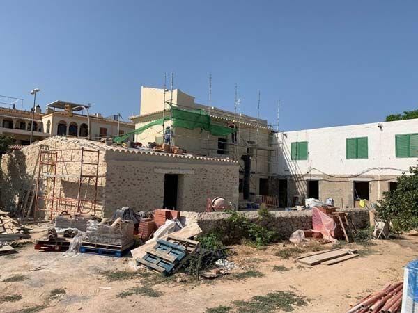 Sitio de construcción con un edificio, andamios y escombros bajo un cielo azul.