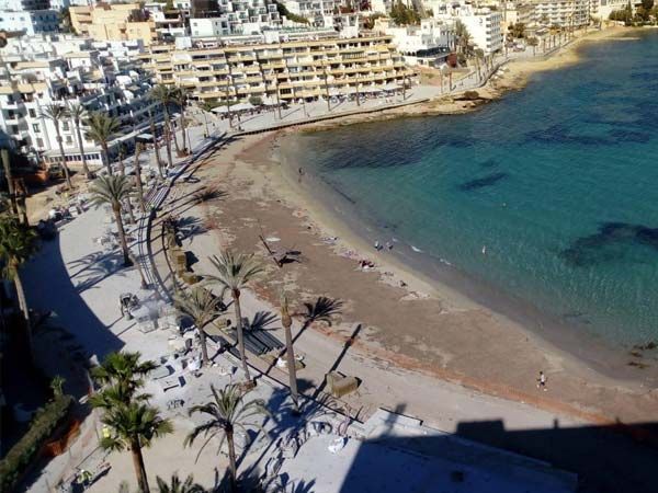 Playa con agua turquesa, palmeras y edificios a lo largo de la orilla.