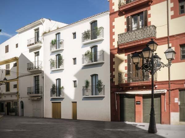 Edificios en una calle española; fachadas blancas y rojas, balcones, farola, cielo azul.