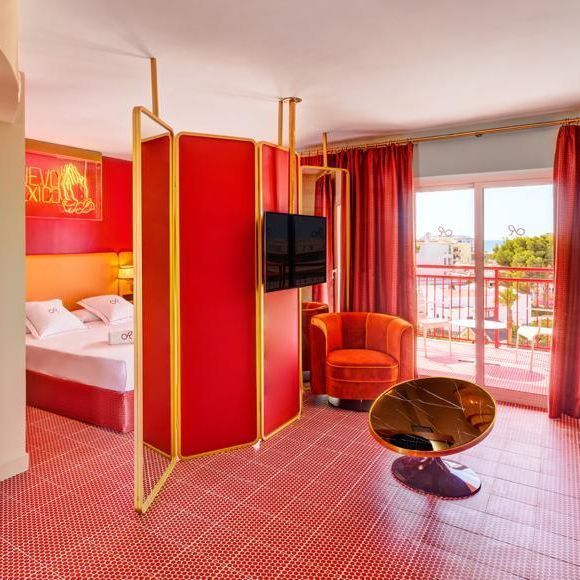 Habitación de hotel roja con cama, biombo rojo, sillón y acceso al balcón.