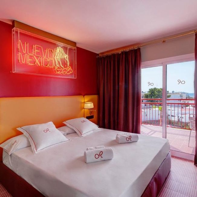 Habitación de hotel con cama doble, paredes rojas y balcón.