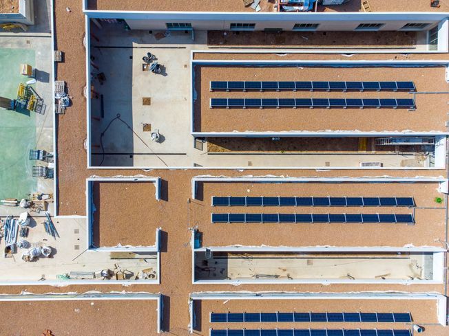 Vista aérea de un edificio con paneles solares en el tejado. Techos marrones, paneles azules y maquinaria de construcción.