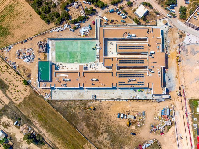 Vista aérea de un edificio en construcción con campo deportivo y zona de aparcamiento.