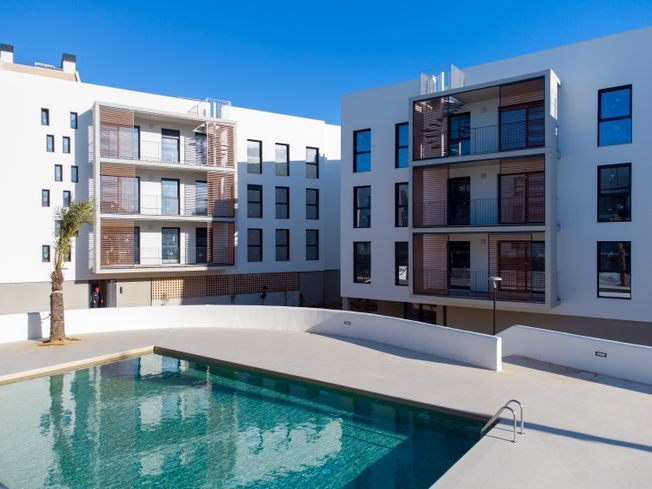 Moderno complejo de apartamentos blancos con piscina turquesa y pasarelas al aire libre.