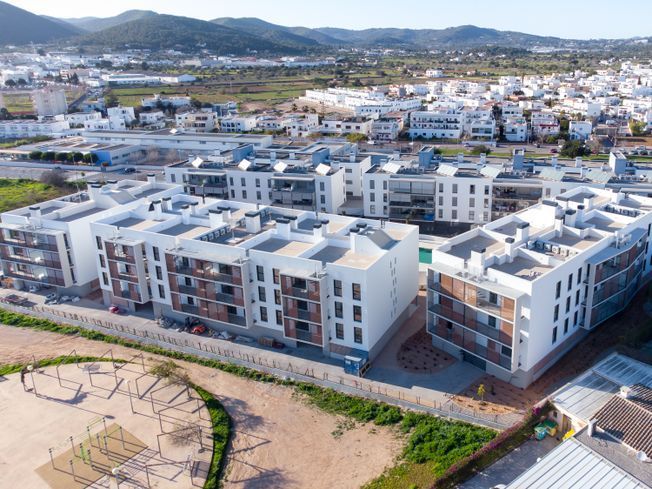 Vista aérea de edificios de apartamentos blancos con balcones marrones en una ciudad, con un parque y montañas distantes.