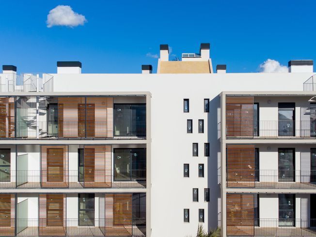 Edificio de apartamentos blanco con contraventanas de madera contra un cielo azul brillante y una sola nube.