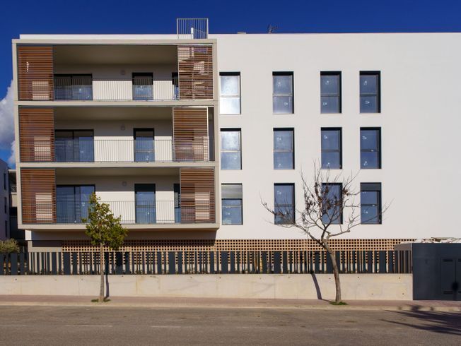 Edificio moderno de color blanco, con balcones, mamparas de madera y valla de hierro forjado.