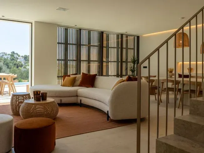 Moderna sala de estar con sofá curvo, persianas de madera y zona de comedor con escalera.