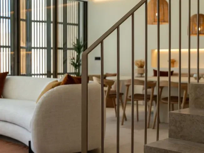 Interior con sofá blanco curvo, comedor abierto y escalera con barandilla de metal.