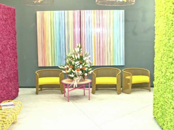 Una colorida sala de espera con una gran obra de arte, sillas amarillas y arreglos florales.