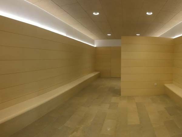 Una zona de spa de color beige, bien iluminada, con bancos, paredes revestidas de madera e iluminación empotrada.