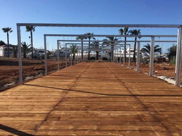 Pasarela de madera con marcos cuadrados de metal, palmeras y cielo azul claro.